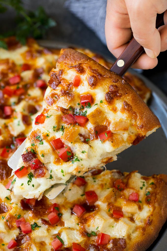 Chicken Alfredo Pizza Recipe #pizza #chicken #bacon #dinner #bajap A hand holding a spatula with a piece of chicken Alfredo pizza on it.
