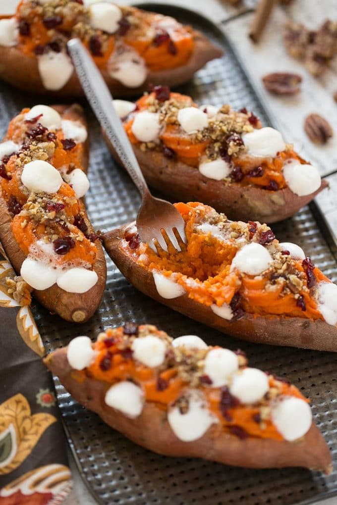Several twice baked sweet potatoes with a fork and some of the mashed potato filling removed. 