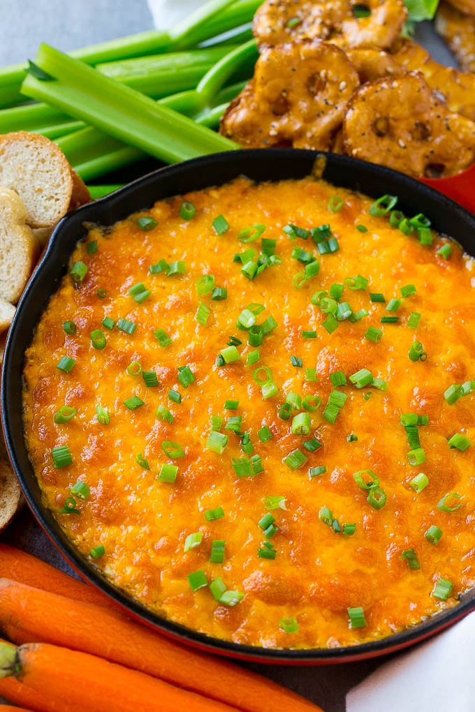 Buffalo Ranch Chicken Dip | Buffalo Chicken Dip | Baked Buffalo Dip | Cheesy Buffalo Dip #buffalowings #buffalochicken #dip #lowcarb #appetizer #bajap Buffalo ranch chicken dip topped with melted cheese and green onions, surrounded by vegetables, pretzels and baguette slices.