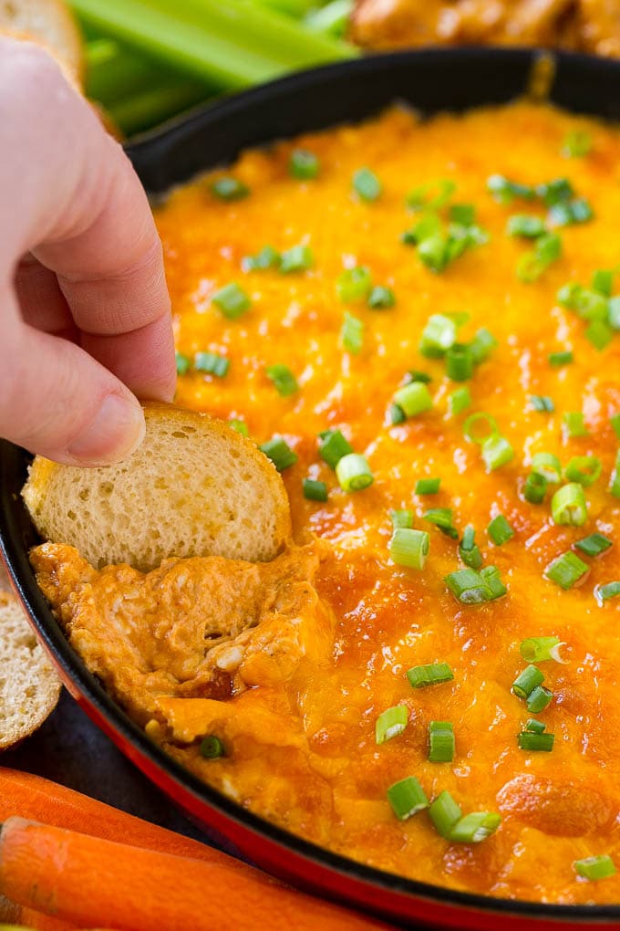 Buffalo Ranch Chicken Dip | Buffalo Chicken Dip | Baked Buffalo Dip | Cheesy Buffalo Dip #buffalowings #buffalochicken #dip #lowcarb #appetizer #bajap Baked buffalo chicken dip with a baguette slice scooping some out.