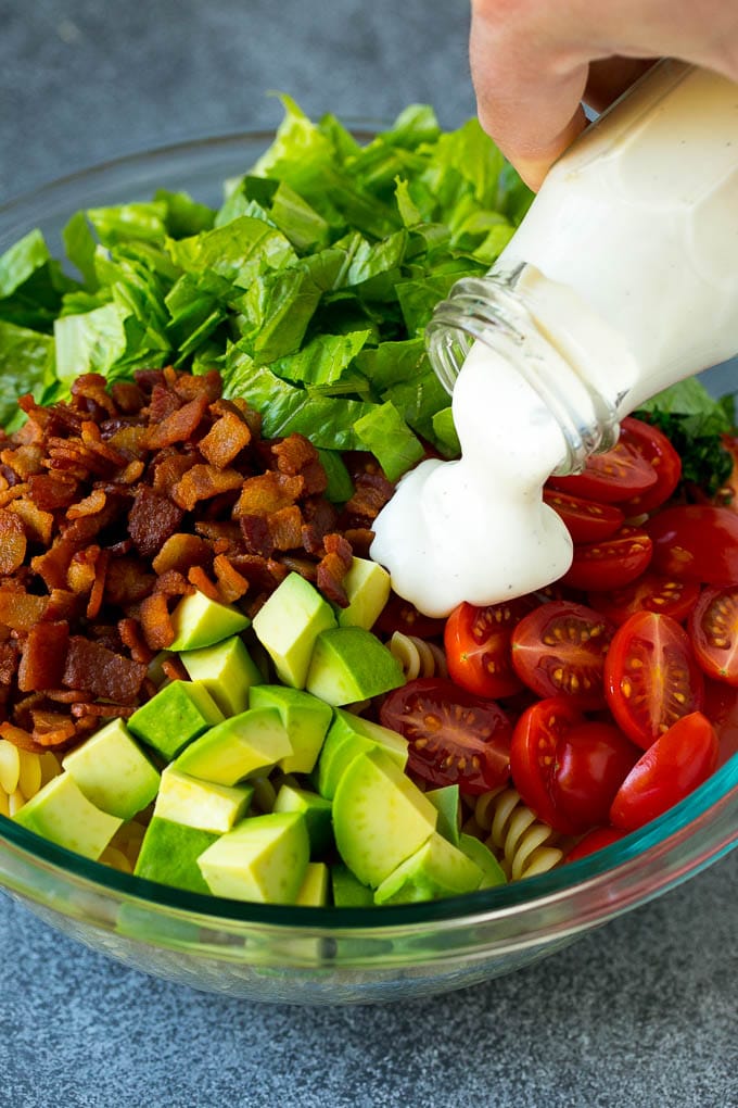 BLT Pasta Salad Recipe | Easy Pasta Salad | Bacon Pasta Salad #salad #pasta #blt #bacon #avocado #dinner #bajap Ranch dressing being poured over tomatoes, lettuce, bacon and avocado.