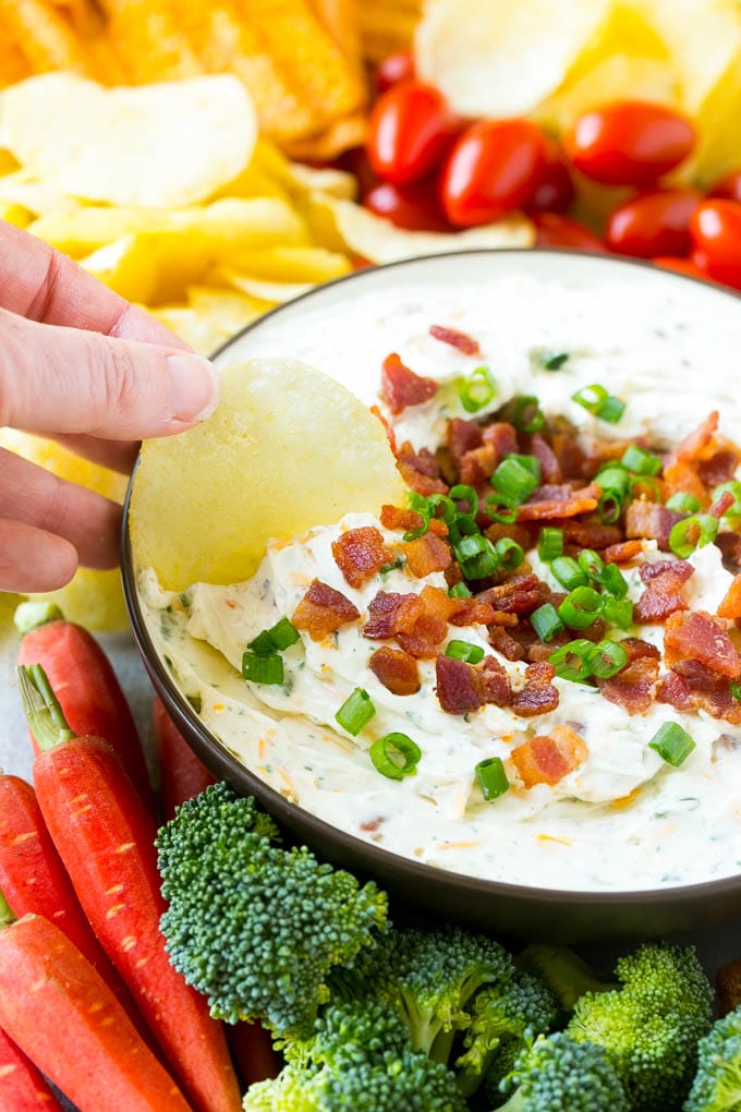Bacon Ranch Dip Recipe | Homemade Ranch Dip | Easy Dip Recipe | Cheddar Ranch Dip #ranch #ranchdip #bacondip #dip #snack #bajap #baconranchdip A hand scooping up bacon ranch dip with a potato chip.