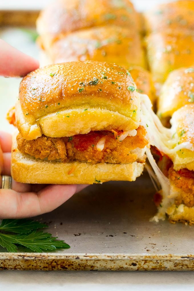 Chicken Parmesan Sliders | Chicken Parmesan Sandwich Recipe | Slider Sandwich Recipe #sliders #chickenparm #chickenparmesan #chickenparmesansliders #dinner #appetizer #bajap A crispy chicken parmesan slider being pulled away by a hand.