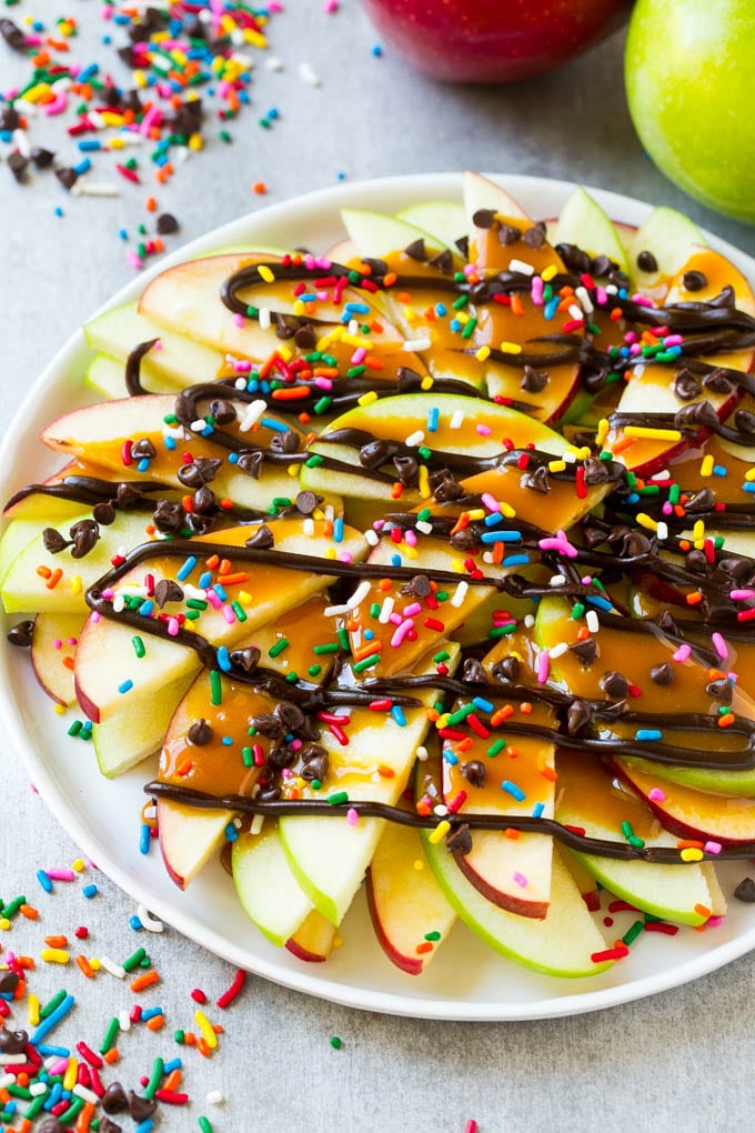 Apple Nachos Recipe | After School Snack | Caramel Apples #apple #apples #caramelapple #snack #dessert #bajap A plate of sliced apple nachos topped with caramel and chocolate sauces, rainbow sprinkles and mini chocolate chips