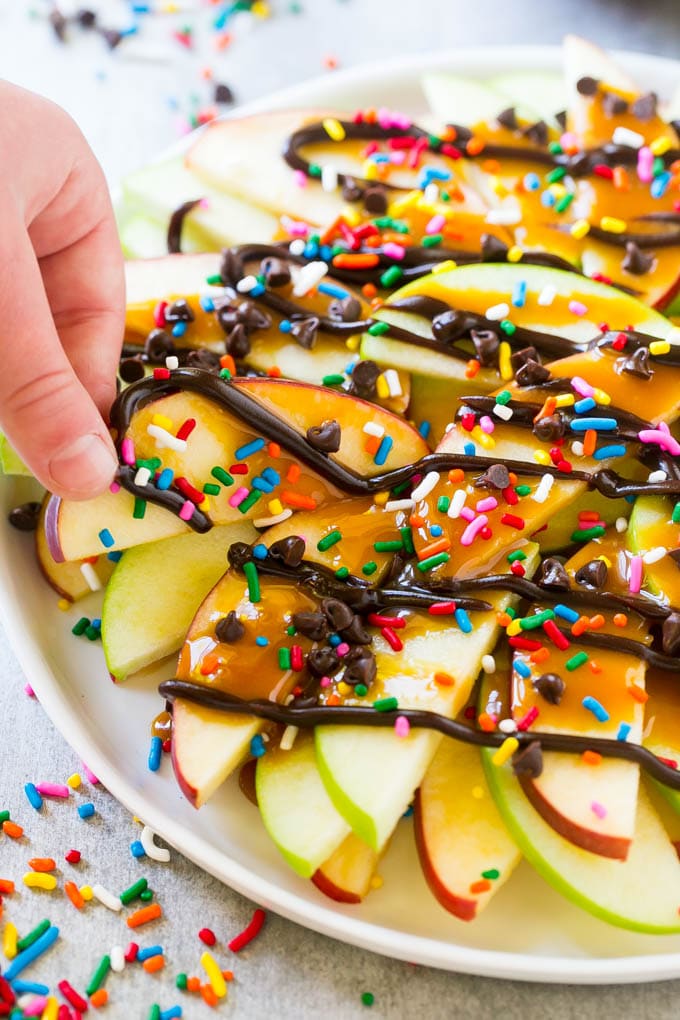 Apple Nachos Recipe | After School Snack | Caramel Apples #apple #apples #caramelapple #snack #dessert #bajap A plate of caramel apple nachos with a hand reaching out to take one.