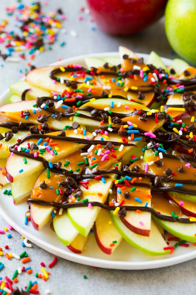 Apple Nachos Recipe | After School Snack | Caramel Apples #apple #apples #caramelapple #snack #dessert #bajap A plate of red and green sliced apples drizzled with caramel and chocolate, then topped with rainbow sprinkles and chocolate chips.