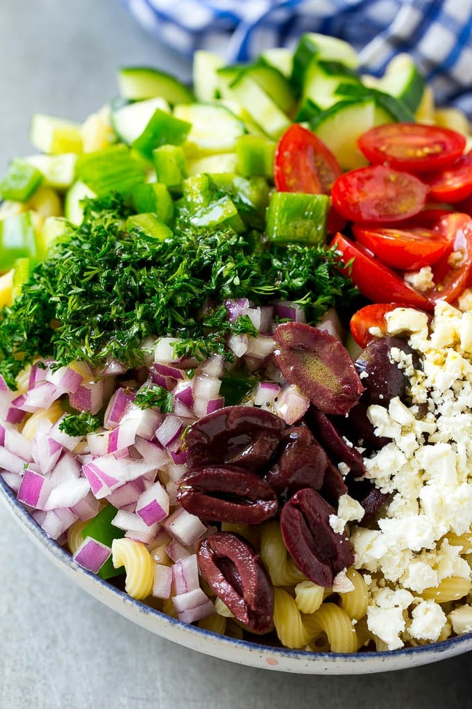 Greek Pasta Salad | Easy Pasta Salad | Vegetable Pasta Salad #pasta #salad #greek #cucumber #tomato #vegetarian #dinner #bajap A bowl of pasta with red onion, kalamata olives, bell pepper and tomatoes, with a drizzle of Greek dressing.