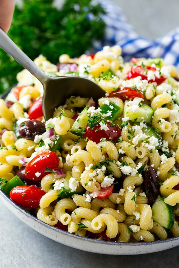 Greek Pasta Salad | Easy Pasta Salad | Vegetable Pasta Salad #pasta #salad #greek #cucumber #tomato #vegetarian #dinner #bajap A bowl of Greek pasta salad with a serving spoon in it.