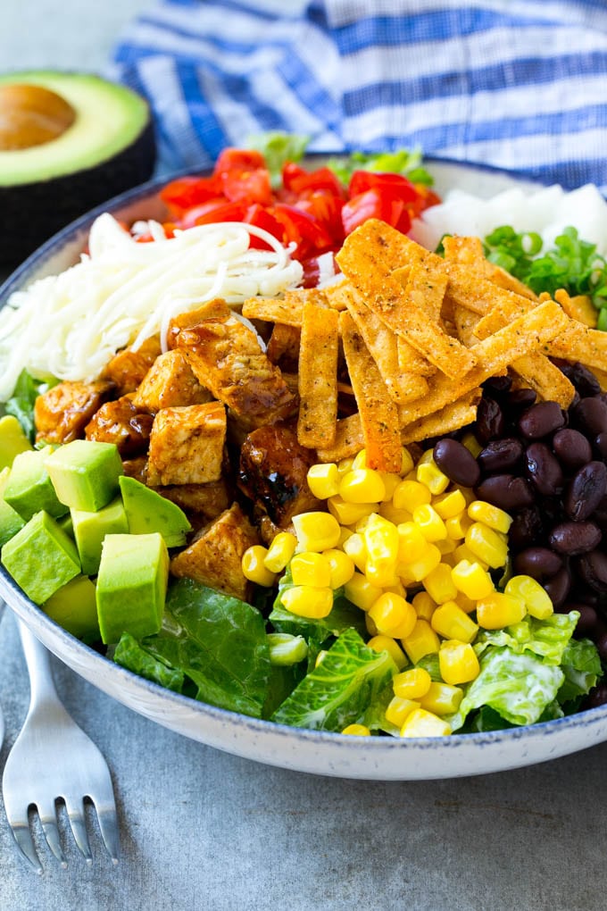 BBQ Chicken Salad Recipe | Chopped BBQ Chicken Salad | CPK Copycat Recipe | California Pizza Kitchen Copycat Recipe | Chicken Ranch Salad #copycat #CPK #BBQchicken #chicken #salad #dinner #bajap A bowl of salad topped with chicken, tortilla strips, black beans, jiacama, avocado and tomatoes.