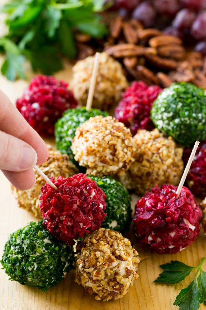 Cheese Ball Bites Recipe | Holiday Cheese Ball Recipe | Pecan Cheese Ball | Cranberry Cheese Ball | Mini Cheese Balls #cheeseball #cheese #appetizer #bajap A hand reaching for an appetizer crusted in dried craberries.