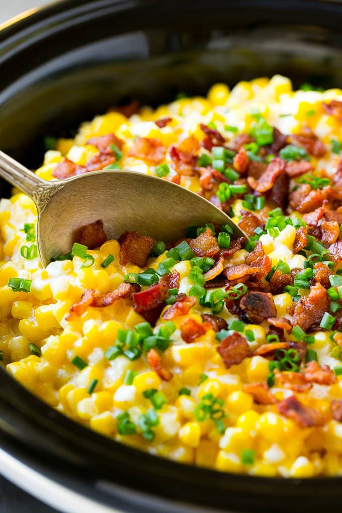 Slow Cooker Creamed Corn Recipe | Easy Creamed Corn Recipe | Slow Cooker Creamed Corn with Bacon | Southern Creamed Corn | Creamed Corn with Cream Cheese #creamedcorn #corn #bacon #crockpot #slowcooker #dinner #bajap A serving spoon in a crock pot full of creamed corn.