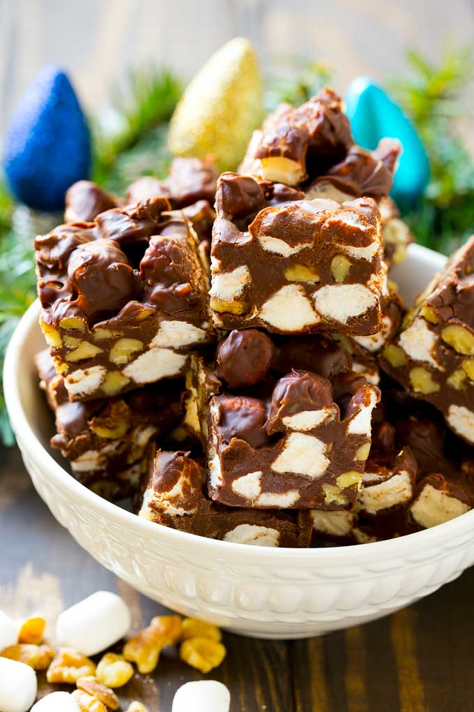 Rocky Road Fudge | Chocolate Marshmallow Fudge | Chocolate Nut Fudge | Microwave Fudge #fudge #chocolatefudge #nobake #chocolate #dessert #rockyroad #bajap A bowl of fudge squares with holiday decorations in the background.