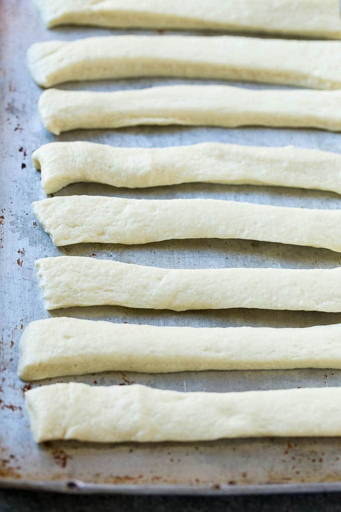 Garlic Knots Recipe | Garlic Rolls | Garlic Butter Rolls | Garlic Bread Recipe #garlic #garlicbread #garlicknots #breadsticks #bajap Strips of pizza dough on a sheet pan that are ready to be tied up.