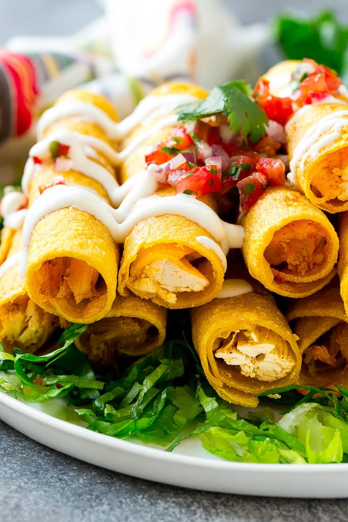 Chicken Taquitos Recipe | Baked Chicken Taquitos | Fried Chicken Taquitos | Mexican Appetizer | Chicken Tortillas #taquitos #chicken #appetizer #tortillas #mexicanfood #bajap A plate of chicken taquitos on a bed of lettuce, topped with sour cream and pico de gallo.