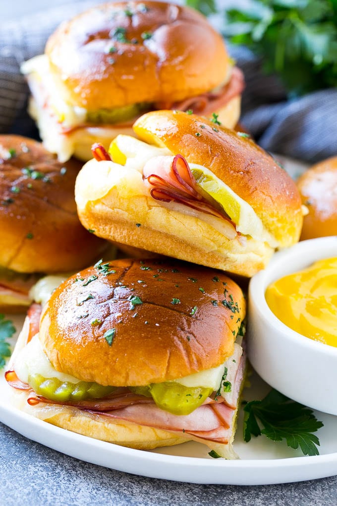 Cuban Sliders Recipe | Cuban Sandwich Recipe | Slider Sandwiches | Ham and Cheese Sliders #sliders #sandwiches #ham #cheese #appetizer #bajap A plate full of Cuban sliders with cheese, pickles and ham on buns.