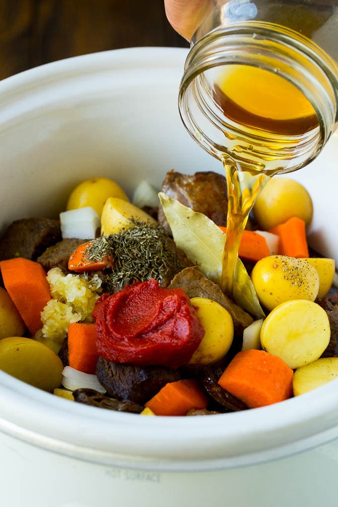 Slow Cooker Beef Stew Recipe | Crockpot Beef Stew #stew #soup #beef #slowcooker #crockpot #dinner #bajap Broth being poured into a slow cooker filled with beef and vegetables.