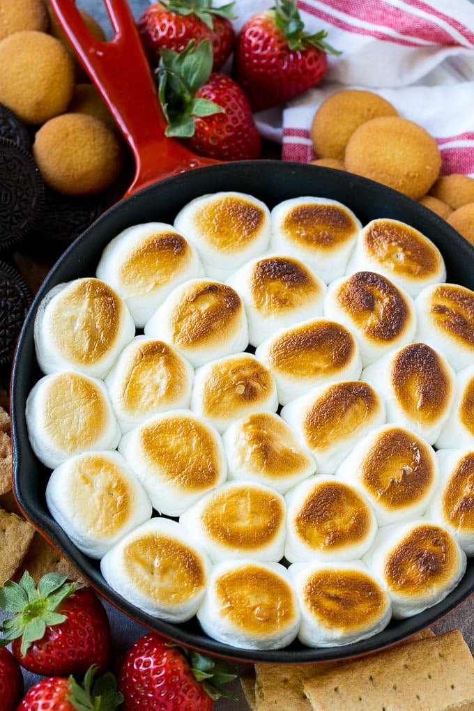 S'mores Dip Recipe | S'mores Skillet | Baked S'mores #smores #dip #chocolate #marshmallow #dessert #bajap A skillet of s'mores dip with melted chocolate chips and toasted marshmallows, surrounded by graham crackers, cookies and strawberries.