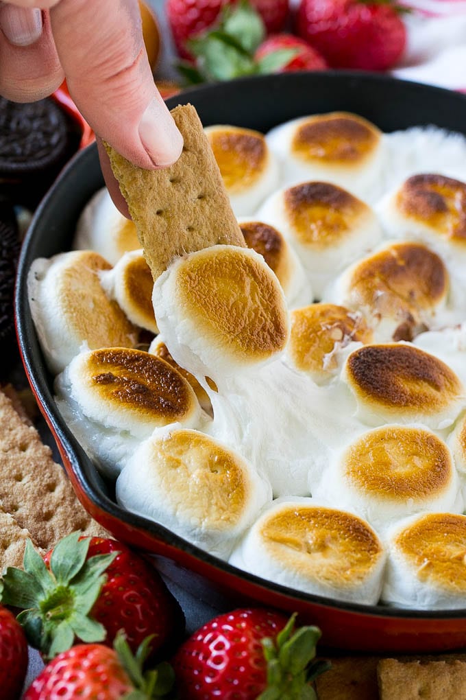 S'mores Dip Recipe | S'mores Skillet | Baked S'mores #smores #dip #chocolate #marshmallow #dessert #bajap A graham cracker topped with melted marshmallow dipping into a skillet of s'mores dip.