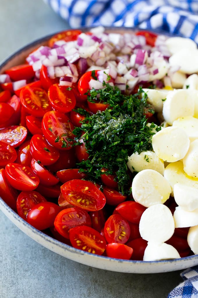 Cherry Tomato Salad Recipe | Tomato Mozzarella Salad | Caprese Salad | Tomato Salad #tomatoes #salad #tomatosalad #caprese #bajap Cherry tomatoes, herbs, mozzarella balls and red onion drizzled with dressing in a bowl.