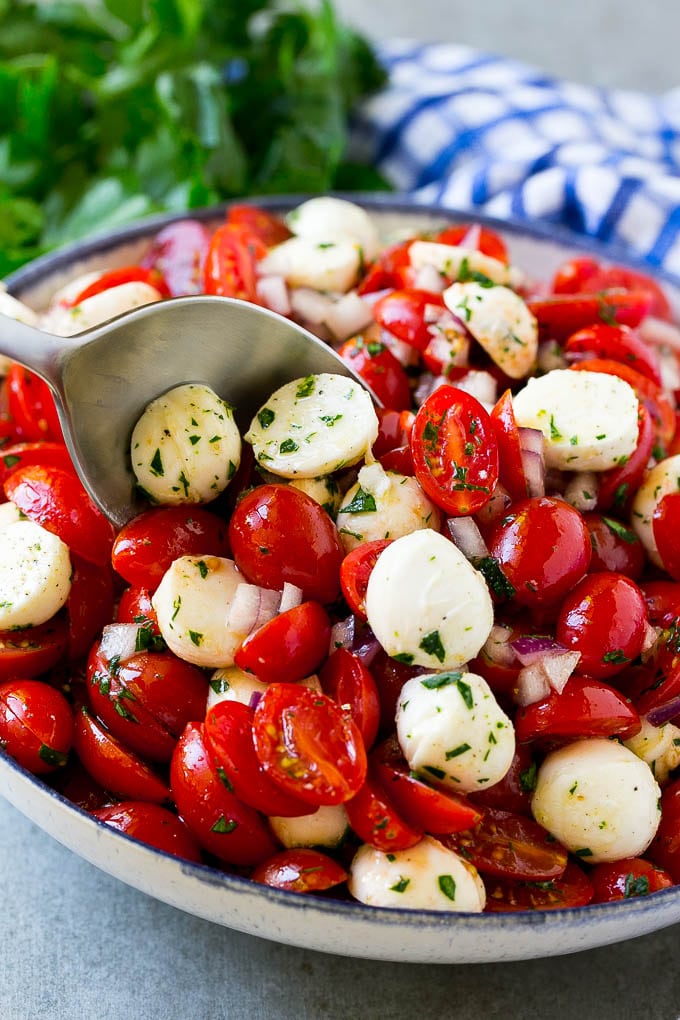 Cherry Tomato Salad Recipe | Tomato Mozzarella Salad | Caprese Salad | Tomato Salad #tomatoes #salad #tomatosalad #caprese #bajap A bowl of cherry tomato salad with a serving spoon in it.