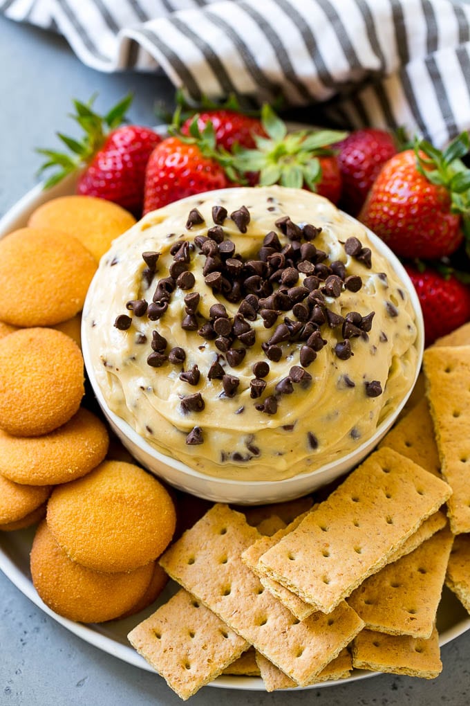 Cookie Dough Dip Recipe | Edible Cookie Dough | Chocolate Chip Cookie Dip #cookies #dip #cookiedough #dessert #snack #bajap A bowl of cookie dough dip topped with chocolate chips and served with cookies and fruit for dipping.