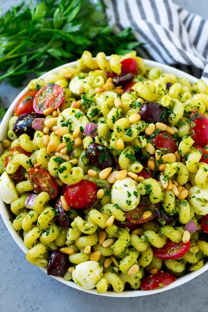 Pesto Pasta Salad | Italian Pasta Salad | Easy Pasta Salad #pasta #salad #pesto #olives #tomatoes #bajap A bowl of pesto pasta salad topped with pine nuts and chopped parsley.