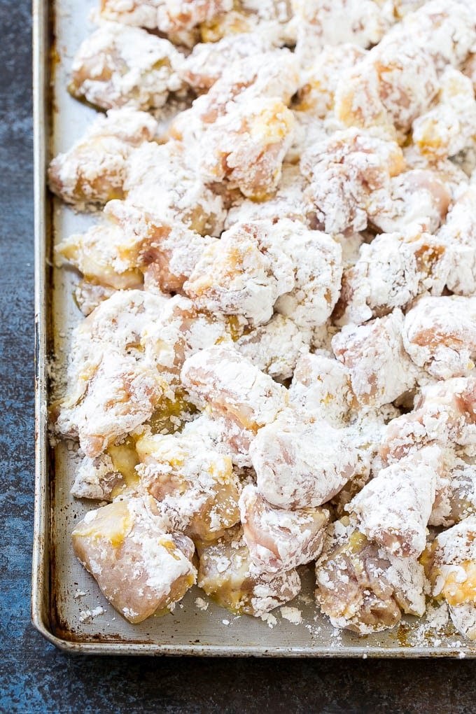 Sweet and Sour Chicken Recipe | Chinese Food Copycat Recipe | Chicken with Pineapple #chicken #chinesefood #pineapple #stirfry #takeout #dinner #bajap Chicken pieces coated in egg and flour on a baking sheet.