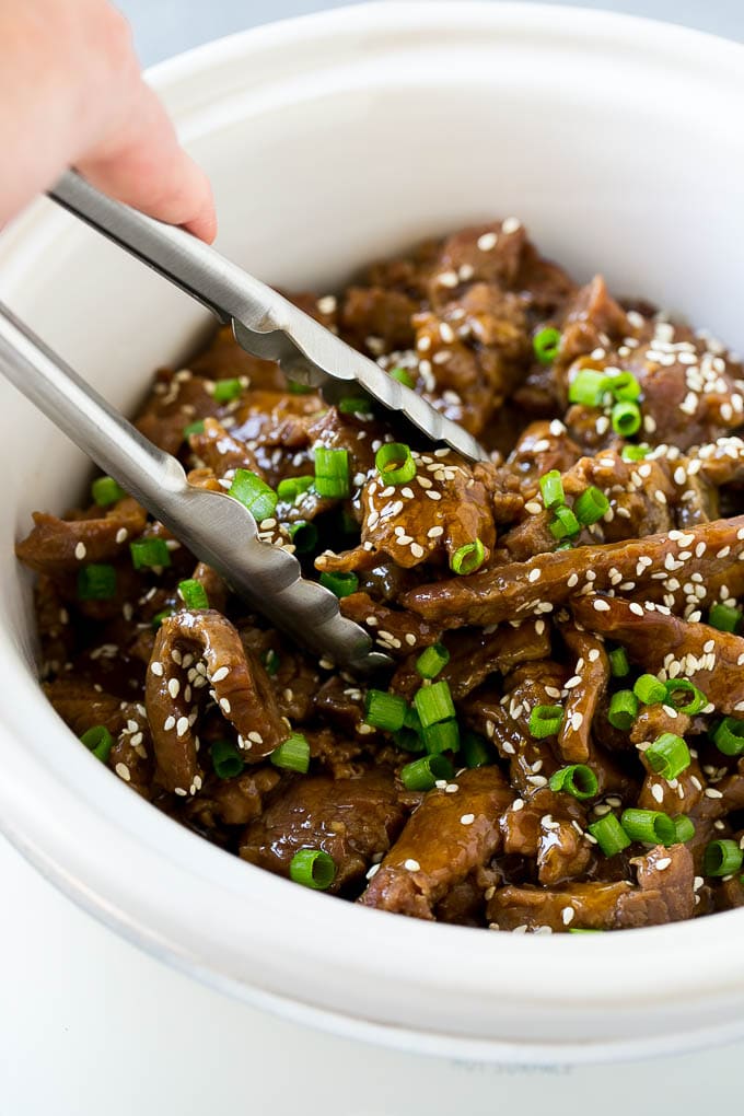 Slow Cooker Korean Beef Recipe | Korean Beef | Flank Steak Recipe #dinner #beef #slowcooker #crockpot #asian #bajap A crock pot of Korean beef with serving tongs in it.