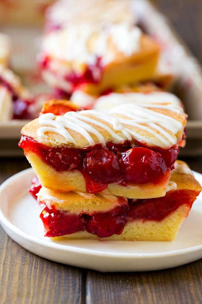 Cherry Bars Recipe | Cherry Pie Bars | Cherry Cookies | Bar Cookies #cookies #bars #cherry #baking #dessert #sweets #bajap Two cherry bars on a plate with a pan of bars in the background.