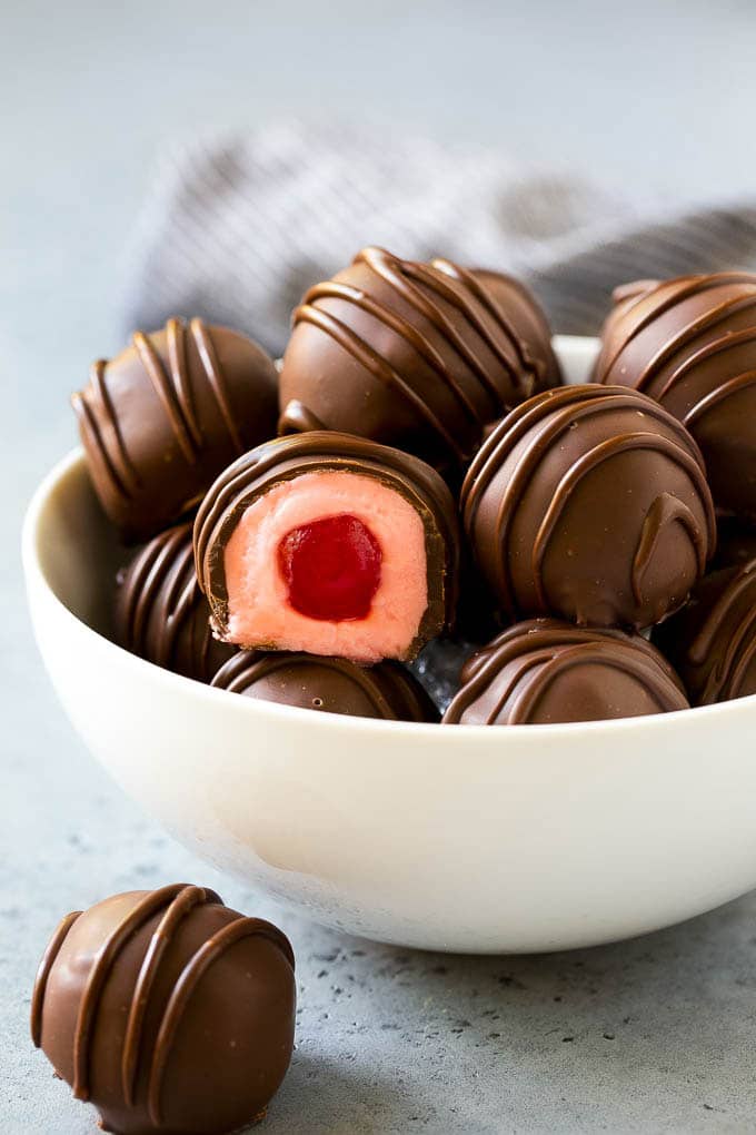 Chocolate Covered Cherries Recipe | Cherry Cordials | Cherry Candy #chocolate #candy #dessert #cherry #sweets #bajap A bowl of chocolate covered cherries with one cut open.
