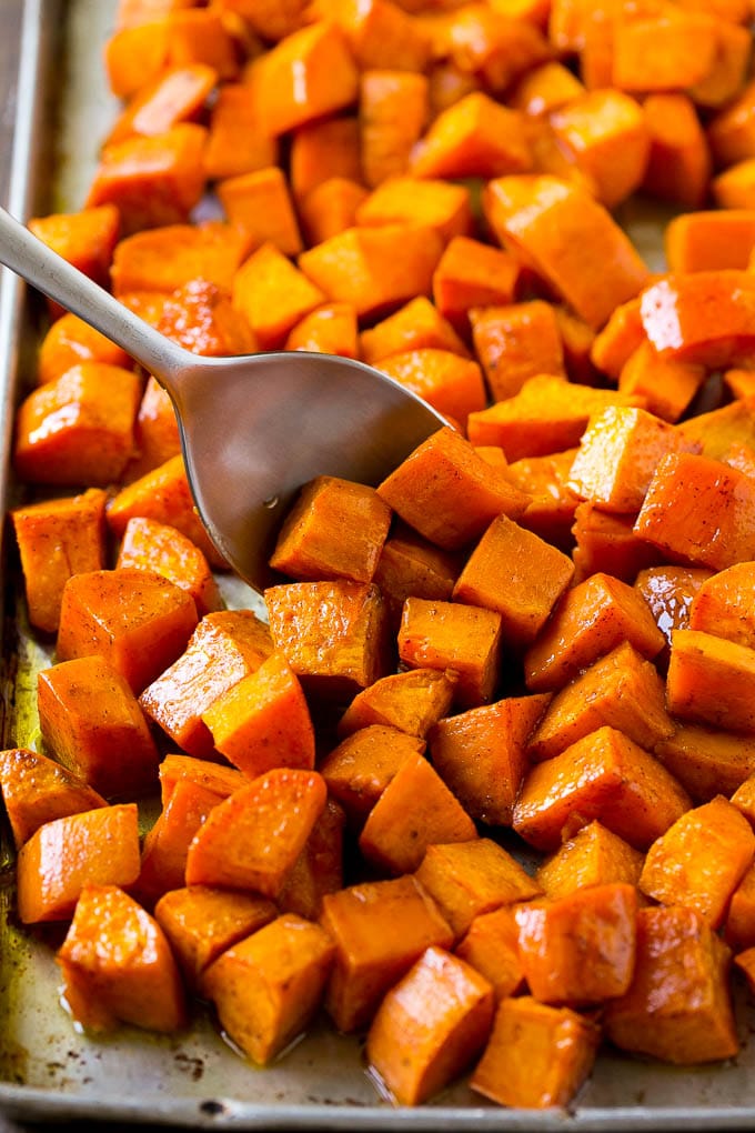 Maple Roasted Sweet Potatoes Recipe | Easy Sweet Potatoes | Baked Sweet Potatoes | Sweet Potato Side Dish #sweetpotatoes #cinnamon #maple #butter #fall #sidedish #dinner #bajap A sheet pan of baked yams flavored with maple and cinnamon, with a serving spoon in them.