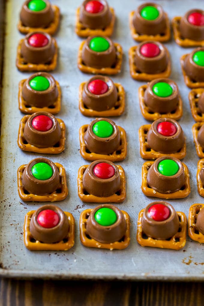 Rolo Pretzels Recipe | Chocolate Pretzels | Caramel Pretzels | Holiday Candy #christmas #baking #dessert #candy #chocolate #caramel #pretzels #bajap Treats with red and green M&M's pressed on top all on a baking sheet.