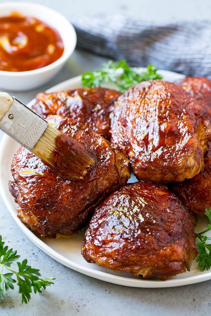 A plate of smoked chicken thighs being basted with barbecue sauce.