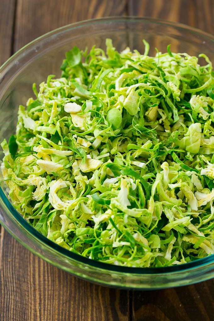 Brussels Sprout Salad Recipe | Shredded Brussels Sprouts Salad | Fall Salad #salad #brusselssprouts #bacon #thanksgiving #pomegranate #apple #dinner #bajap Shredded sprouts in a glass bowl.