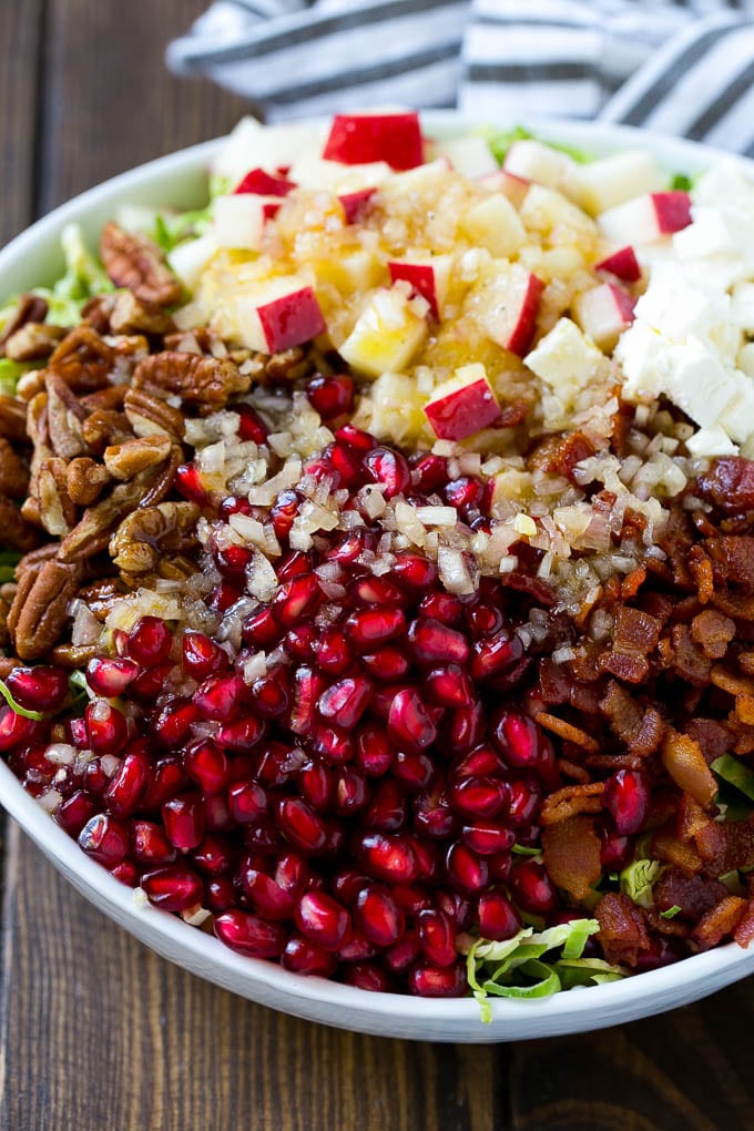 Brussels Sprout Salad Recipe | Shredded Brussels Sprouts Salad | Fall Salad #salad #brusselssprouts #bacon #thanksgiving #pomegranate #apple #dinner #bajap Dressing poured on top of salad that contains sprouts, pomegranate seeds, pecans and bacon.