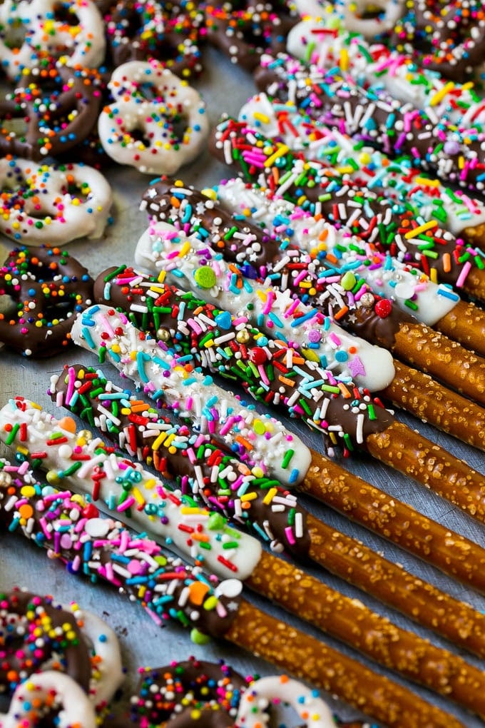 Chocolate Covered Pretzels Recipe | Sprinkle Pretzels | No Bake Dessert #pretzels #chocolate #christmas #sprinkles #candy #bajap A sheet pan with coated twists and rods decorated with rainbow sprinkles.
