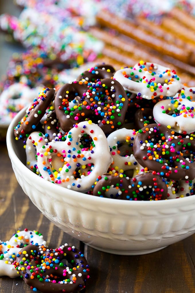 Chocolate Covered Pretzels Recipe | Sprinkle Pretzels | No Bake Dessert #pretzels #chocolate #christmas #sprinkles #candy #bajap A bowl of chocolate covered pretzels decorated with rainbow sprinkles.
