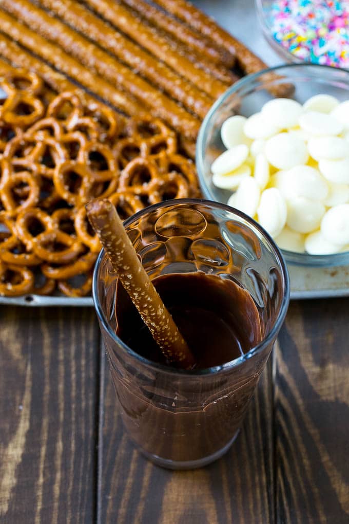 Chocolate Covered Pretzels Recipe | Sprinkle Pretzels | No Bake Dessert #pretzels #chocolate #christmas #sprinkles #candy #bajap A rod in a glass full of melted chocolate.