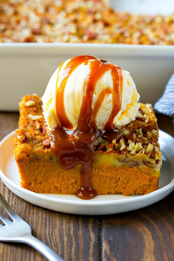 Pumpkin Dump Cake Recipe | Pumpkin Cake | Pumpkin Pie Cake #pumpkin #cake #pecans #fall #thanksgiving #dessert #bajap A slice of pumpkin dump cake topped with ice cream and caramel sauce.