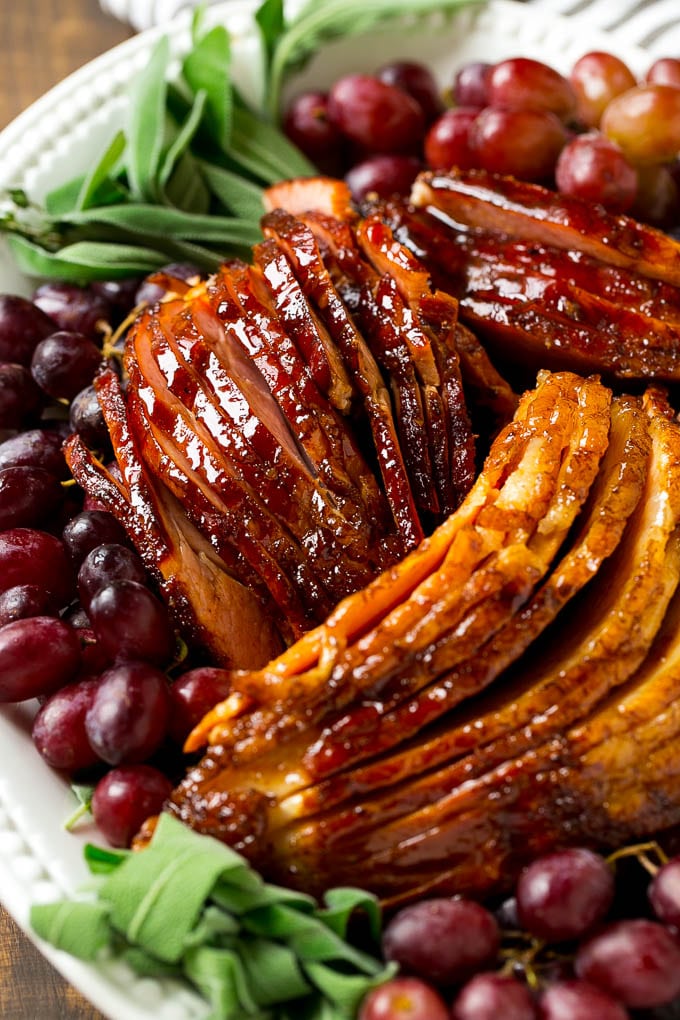 Brown Sugar Smoked Ham Recipe | Holiday Ham Recipe | Brown Sugar Glazed Ham #ham #christmas #thanksgiving #easter #smoker #dinner #brownsugar #bajap #glutenfree Sliced smoked ham on a serving platter, garnished with grapes and fresh herbs.