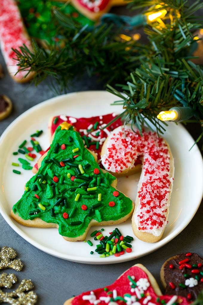 Christmas Sugar Cookies Recipe | Christmas Cookies #cookies #frosting #sprinkles #sugarcookies #christmas #dessert #bajap A selection of Christmas sugar cookies served on a plate, with holiday decorations in the background.