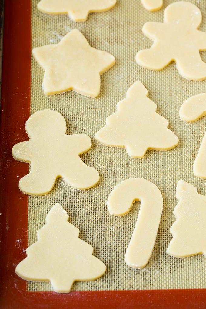 Christmas Sugar Cookies Recipe | Christmas Cookies #cookies #frosting #sprinkles #sugarcookies #christmas #dessert #bajap Cookie dough cut into holiday shapes on a baking sheet.