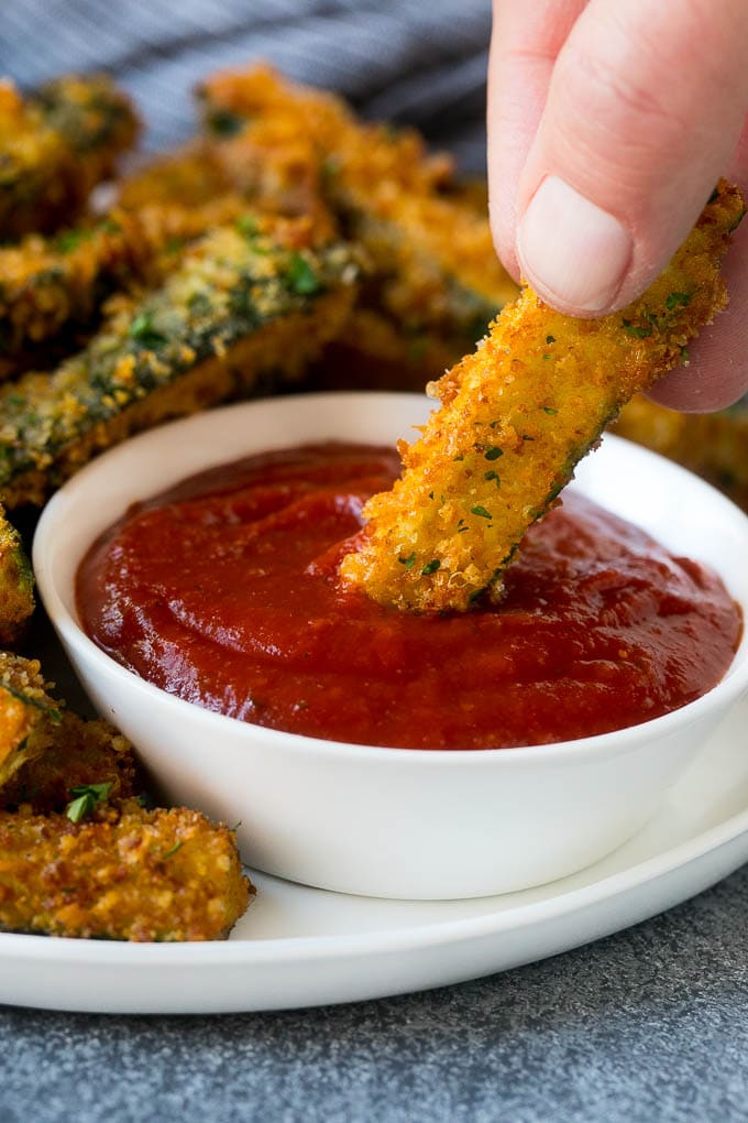 Fried Zucchini Recipe | Zucchini Fries | Zucchini Recipe #appetizer #zucchini #snack #bajap A hand dipping a piece of fried zucchini into marinara sauce.