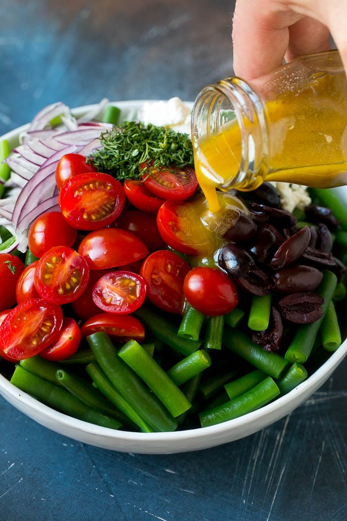 Green Bean Salad Recipe | String Bean Salad | Chopped Salad #greenbeans #tomatoes #olives #salad #cleaneating #lowcarb #glutenfree #bajap Dressing being poured over veggies like cherry tomatoes, olives and onions.