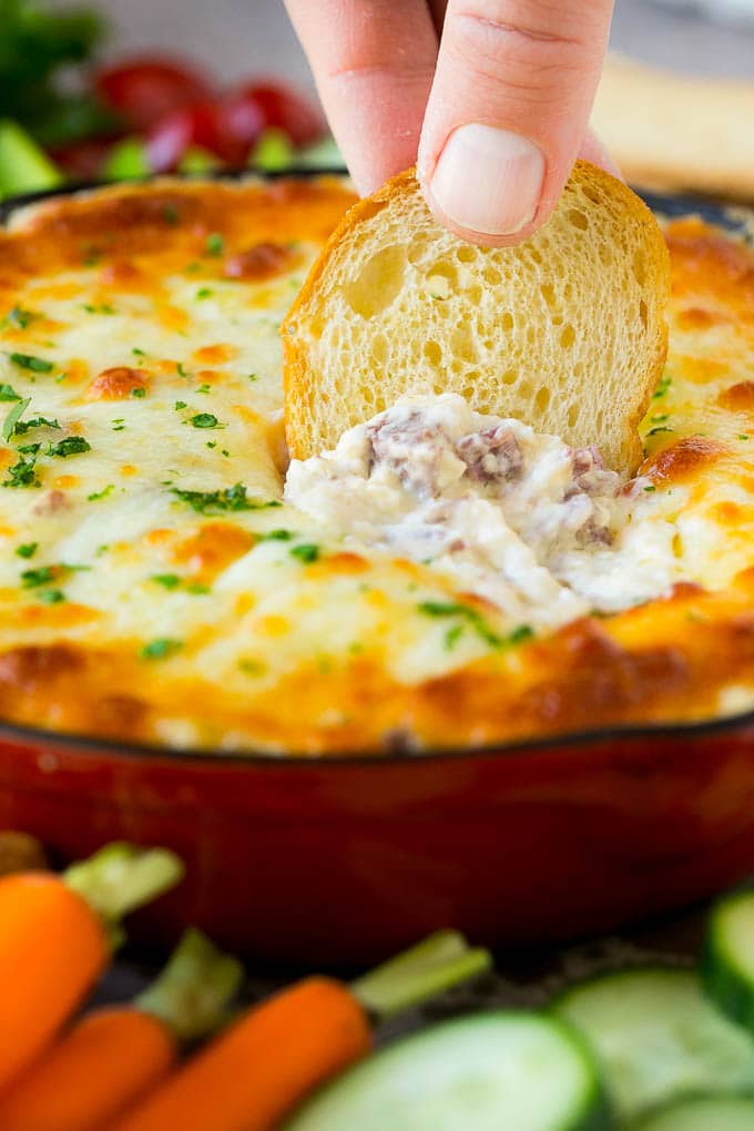 Reuben Dip Recipe | Corned Beef Dip | Cheese Dip #dip #cheese #cornedbeef #appetizer #lowcarb #keto #bajap A baguette chip dipping into a skillet of Reuben dip.