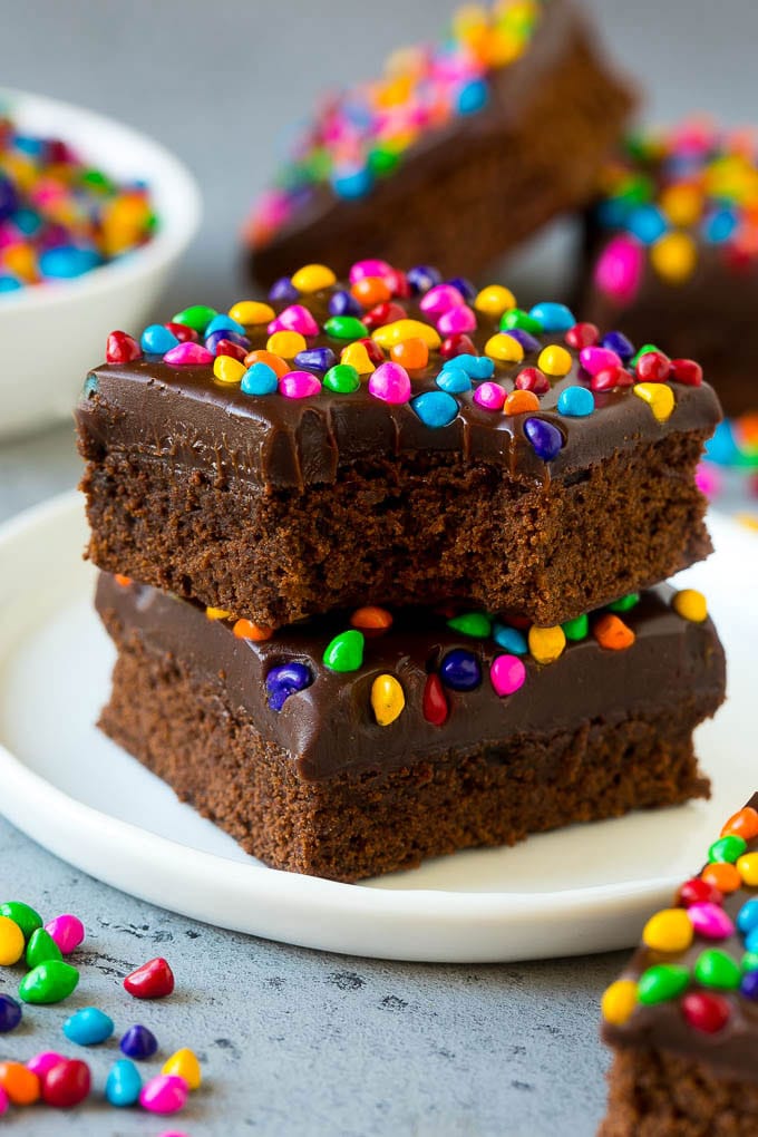 Cosmic Brownies Recipe | Cocoa Brownies | Frosted Brownies #brownies #chocolate #dessert #bajap #sprinkles A stack of cosmic brownies on a plate with a bite taken out of one.