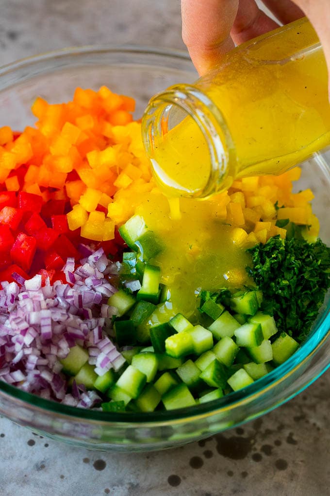 Israeli Salad Recipe | Cucumber Salad | Tomato Salad | Chopped Salad #salad #cleaneating #healthy #glutenfree #lowcarb #keto #sidedish #lunch #bajap Lemon dressing being poured over chopped vegetables.