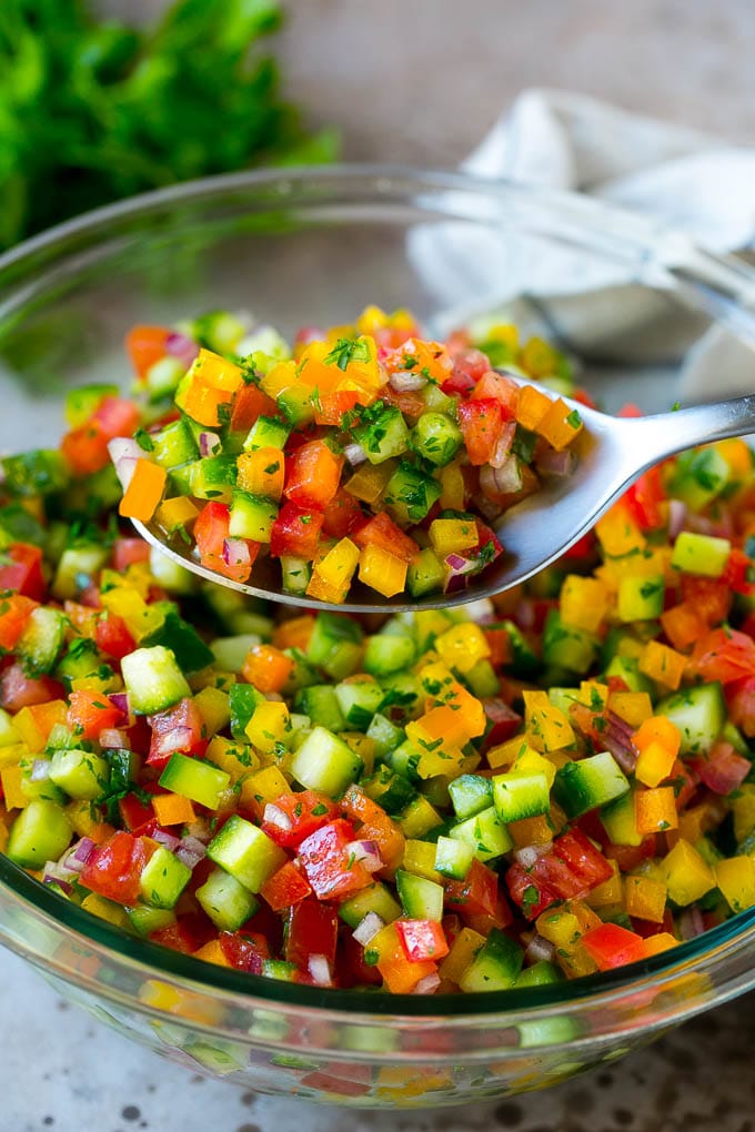 Israeli Salad Recipe | Cucumber Salad | Tomato Salad | Chopped Salad #salad #cleaneating #healthy #glutenfree #lowcarb #keto #sidedish #lunch #bajap A spoon holding up a serving of Israeli salad.
