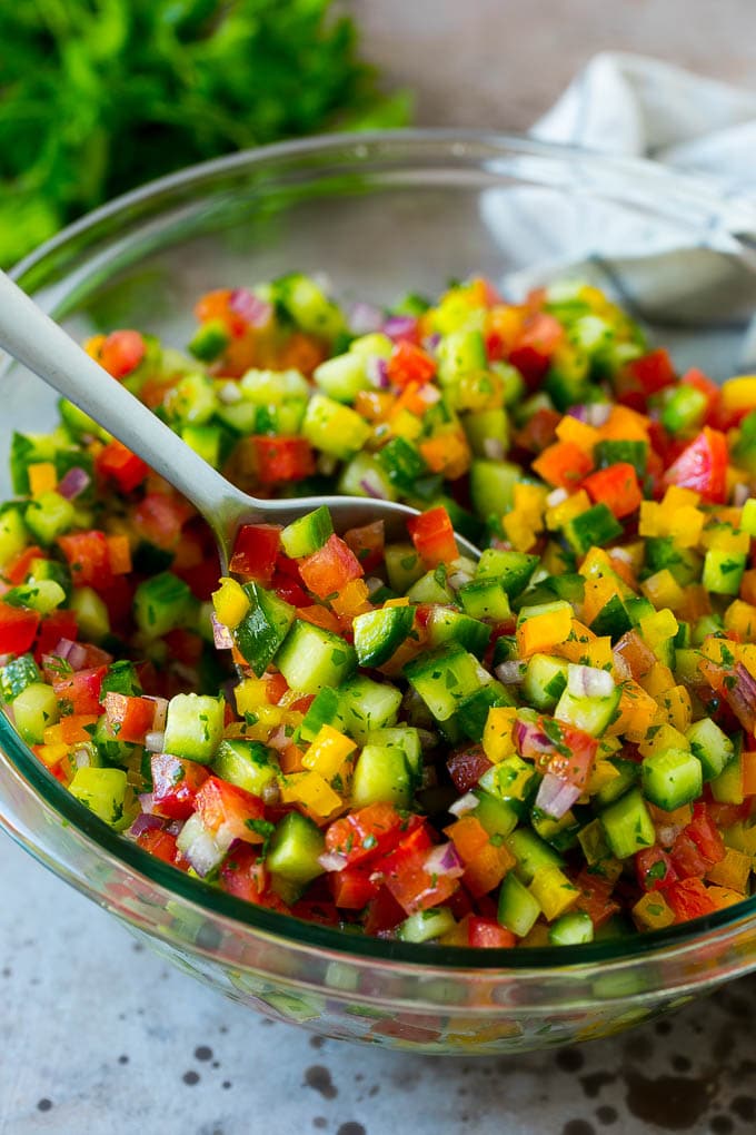 Israeli Salad Recipe | Cucumber Salad | Tomato Salad | Chopped Salad #salad #cleaneating #healthy #glutenfree #lowcarb #keto #sidedish #lunch #bajap A bowl of Israeli salad with a serving spoon in it.