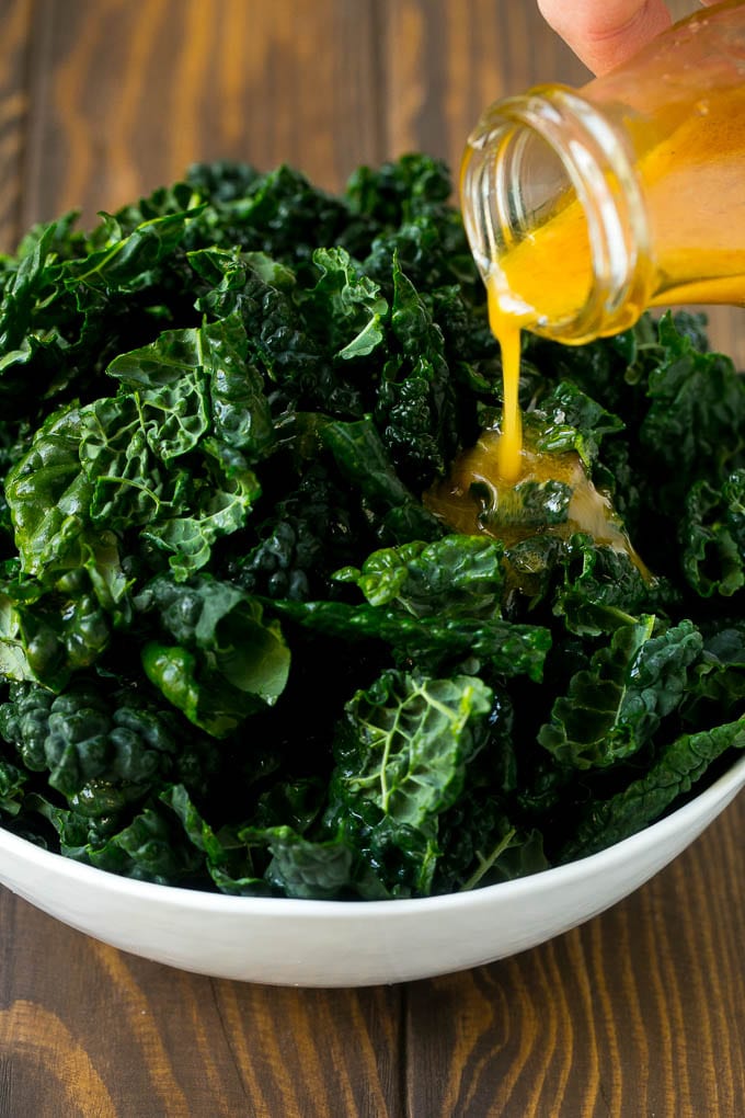 Apple Kale Salad Recipe | Kale Recipe | Fall Salad #kale #apples #bacon #salad #feta #dinner #lunch #bajap Dressing being poured over dinosaur kale leaves.
